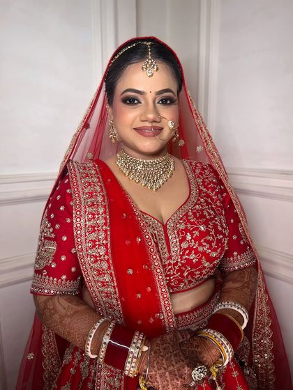The smile of a happy bride says it all. This classic red bridal look is crafted with precision, featuring a smooth, long-lasting base and makeup that enhances her natural beauty.