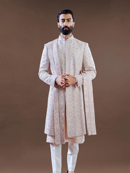 A full-length view of a layered, open-style sherwani in a subtle blush tone. The clean lines and flowing silhouette offer a modern, sophisticated option for the contemporary groom.