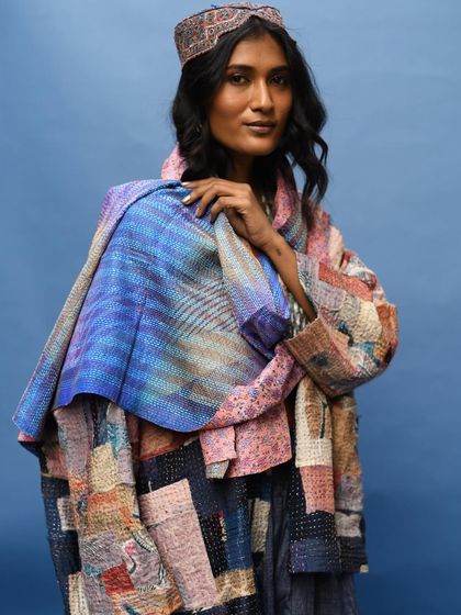 A striking portrait for Wandering Silk, where the model is wrapped in a colorful patchwork jacket and scarf. The deep blue background makes the vibrant colors and textures of the slow fashion pieces pop.