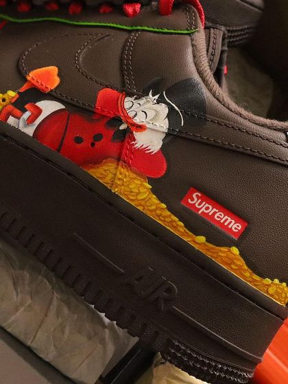 A close-up of Scrooge McDuck on the heel of the AF1s, lounging on his pile of money next to a Supreme logo. It's all about those fun little details.