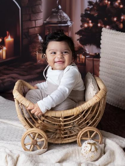 A picture that feels like a warm hug. This cozy Christmas-themed setup with a fireplace backdrop and presents is perfect for holiday milestone photos.