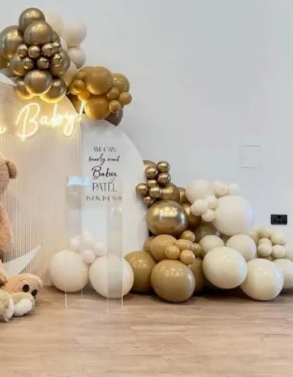 An elegant baby shower setup with an 'Oh Baby' neon sign, chrome gold and neutral balloons, and plush teddy bears.