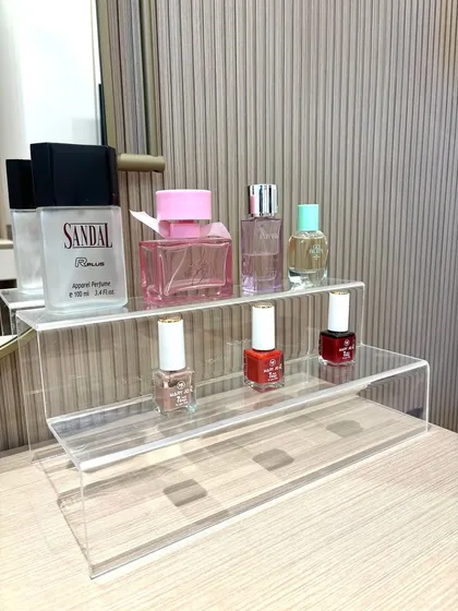 A simple acrylic tiered stand is an elegant way to organize and display perfumes and nail polishes on a vanity, keeping surfaces clear and products visible.