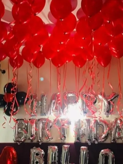 A classic birthday room setup using red and black balloons to cover the ceiling. The silver 'HAPPY BIRTHDAY' foil letters stand out and create a festive focal point in the room.