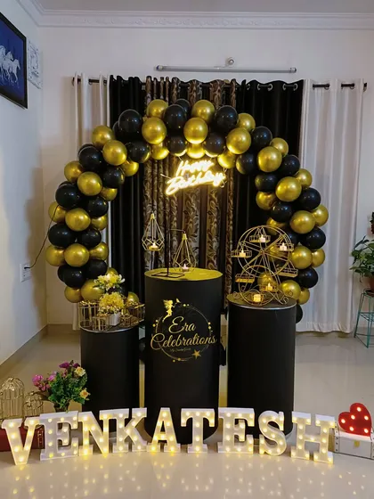 A stylish black and gold birthday setup for Venkatesh. The balloon ring, neon sign, and black plinths make for a very sleek and modern celebration.