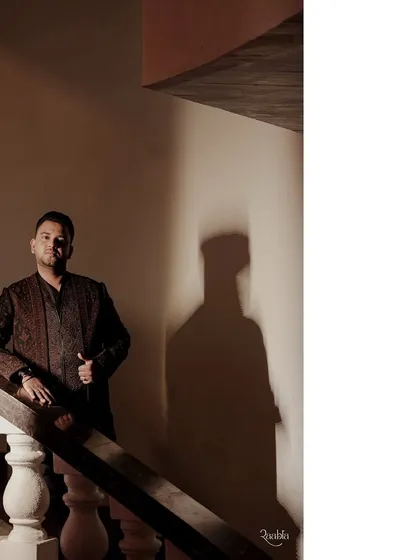 The groom strikes a pose. The play of light and shadow adds a dramatic flair, highlighting the sharp silhouette of his Sangeet outfit.