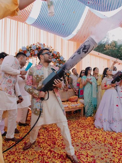 The groom takes charge of the flower cannon, adding to the fun and colorful chaos of the Haldi celebration.