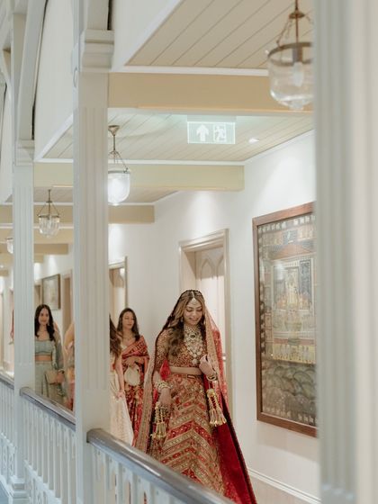 The bride walks down a hallway, followed by her bridesmaids. This candid shot captures the movement and anticipation as she makes her way to the ceremony.