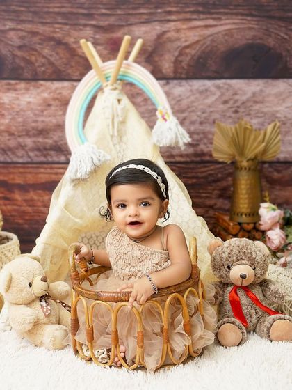 A quiet moment in a teddy bear's paradise. This baby girl looks so sweet and content in a wicker basket, surrounded by her furry friends in a boho-themed setup.