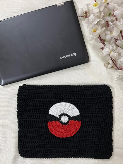 A top-down view of the handmade crochet laptop sleeve, showing the detailed appliqué of the Poké Ball.