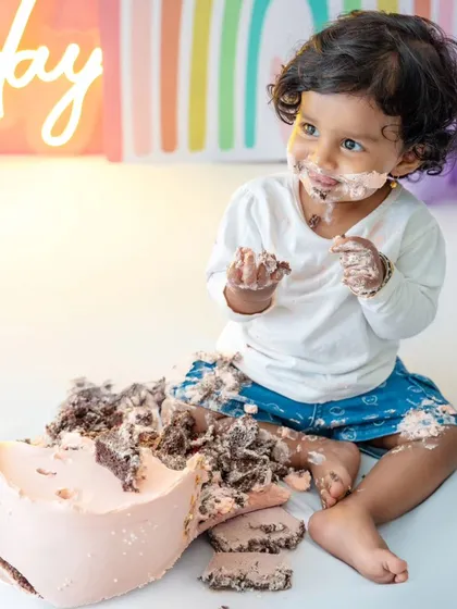 A wider angle of the cake smash, showing the beautiful destruction of the cake and the baby's happy involvement.