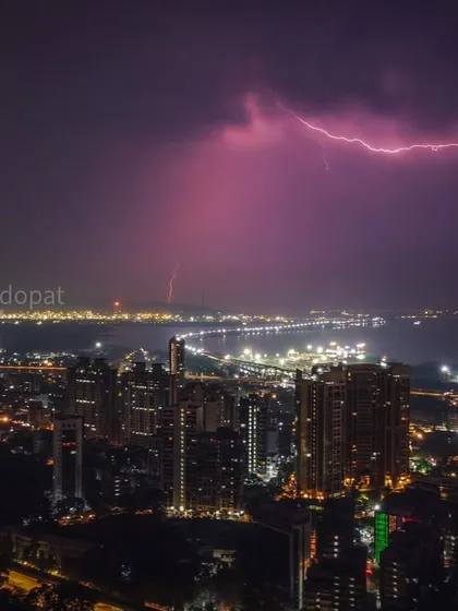 A purple lightning strike captured by drone over the Mumbai coast, with the city lights glowing below.