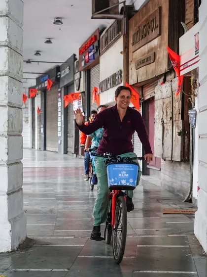 A rider waves as she cycles through the iconic arches of Connaught Place. The wide corridors are perfect for a leisurely ride, soaking in the atmosphere of this famous shopping district.