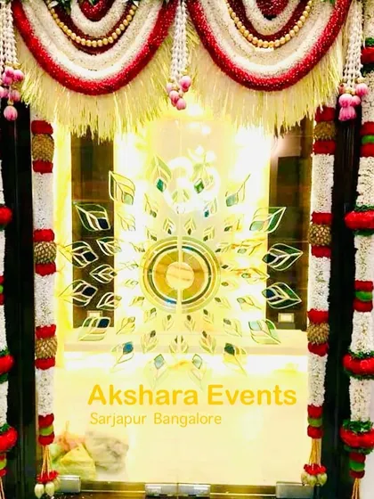 A close-up of a pooja room door decoration. This design features garlands of tuberose and red flowers with lotus bud hangings, framing the glass door.