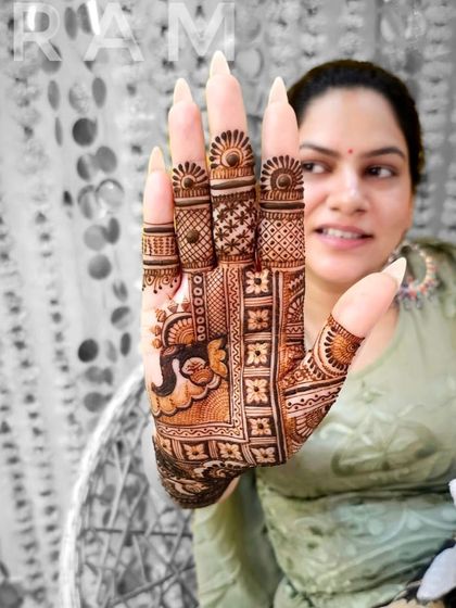 A happy client showing off her detailed mehndi. The design includes a peacock on the palm and intricate patterns covering the fingers and wrist.
