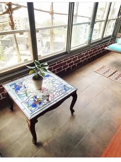A beautiful enclosed balcony, or sunroom, with exposed brick detail and a vintage-style coffee table. This space is perfect for relaxing with a view.