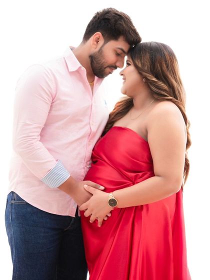 An intimate pose against a clean, white background. The couple's foreheads touch as they hold the baby bump together, creating a simple, powerful image of their bond.