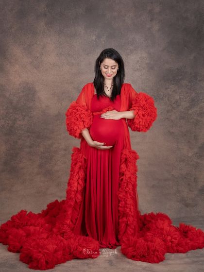 A quiet moment of reflection. This full-length portrait in a dramatic red gown captures the peaceful anticipation of motherhood.