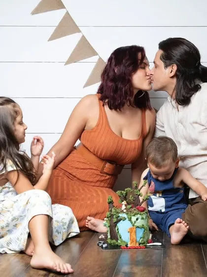 A cake smash is a family affair. This candid moment captures the love and joy surrounding the birthday boy as his parents kiss and his sister looks on.