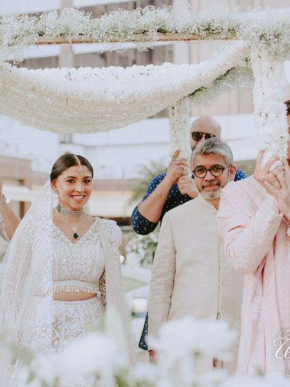 A close-up of the radiant bride during her entry, smiling as she walks under a delicate 'phoolon ki chadar' made of baby's breath.