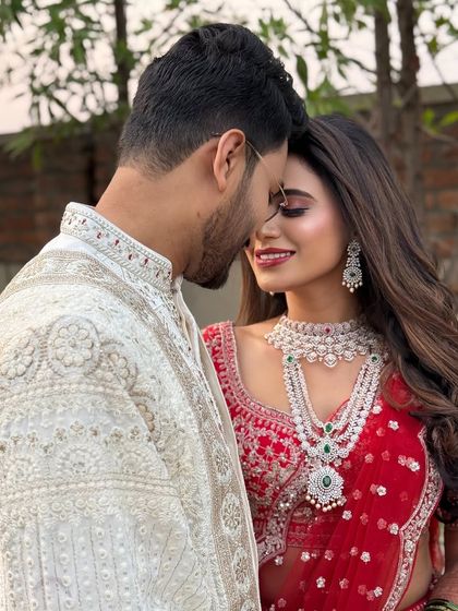 An intimate couple portrait. The bride is wearing a vibrant red lehenga with sparkling diamond jewelry, and her makeup is glamorous with a matching red lip.