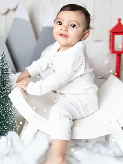 A cozy 'Winter Wonderland' themed session. This little one is dressed in a simple white outfit, sitting amongst fake snow, miniature pine trees, and mountain cutouts.