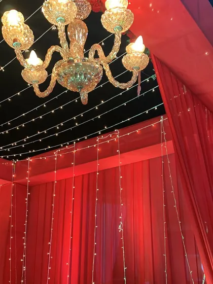 A close-up of the ceiling detail in the red entrance tunnel, showing the crystal chandelier and strings of fairy lights against the dark night sky.