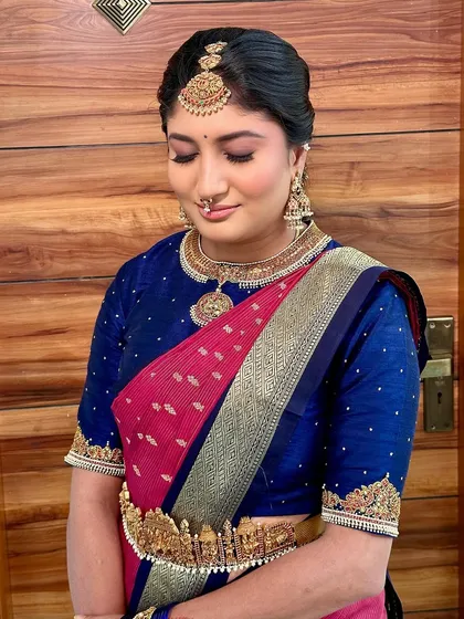 A traditional South Indian look in a pink and blue saree, featuring a stunning temple-style waist belt (vaddanam).