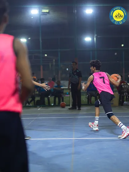 A player drives past a defender during a competitive match. The court comes alive at night with intense, fast-paced basketball action.