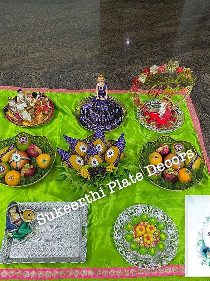 This platter arrangement for an 'Uruthi Varthai' ceremony in Karumathampatti features a mix of dolls, fruits, and sweets, all beautifully presented on a green silk cloth.