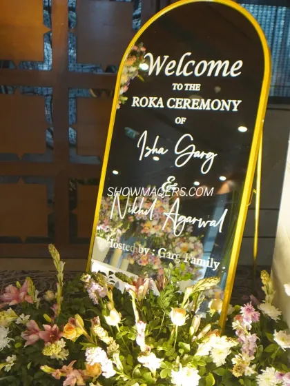 A personalized welcome mirror for Nikhil and Isha's Roka ceremony, surrounded by fresh flowers.