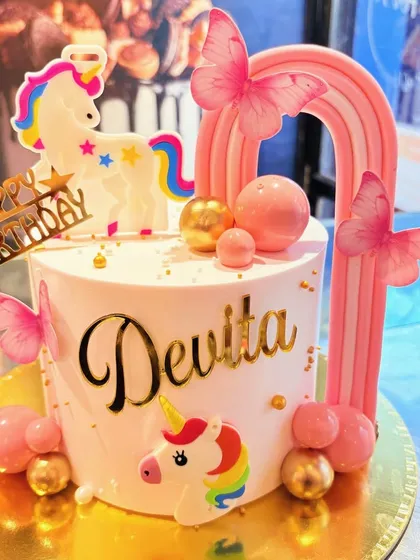 A beautiful unicorn-themed cake with pink butterflies, a rainbow arch, and gold accents.