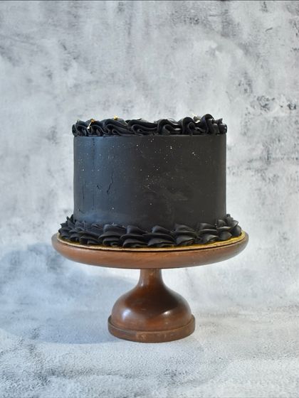 A sleek and modern all-black hazelnut ganache cake. The minimalist design is elevated by the piped ruffle border and a subtle shimmer, perfect for a sophisticated joint birthday celebration.