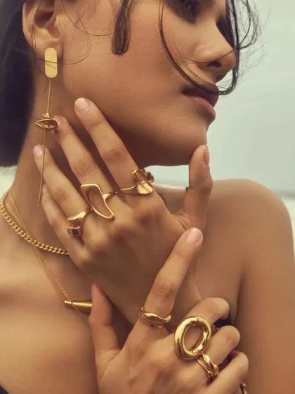 A detailed shot of the layered gold rings and earrings. The makeup is kept minimal to let the accessories be the hero.