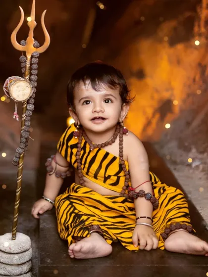 A sweet portrait of a toddler dressed as Lord Shiva, sitting in our cave setup with his trishul.
