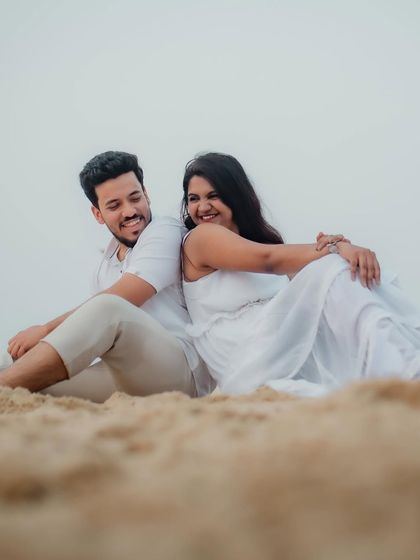 A relaxed and happy pose on the sand. The couple sits back-to-back, sharing a smile, in this beautifully composed shot from their pre-wedding beach session in Kokan.