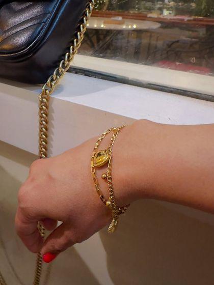 My hand adorned with a layered gold heart bracelet from Palmonas, paired with a classic handbag to show how to style their jewelry.