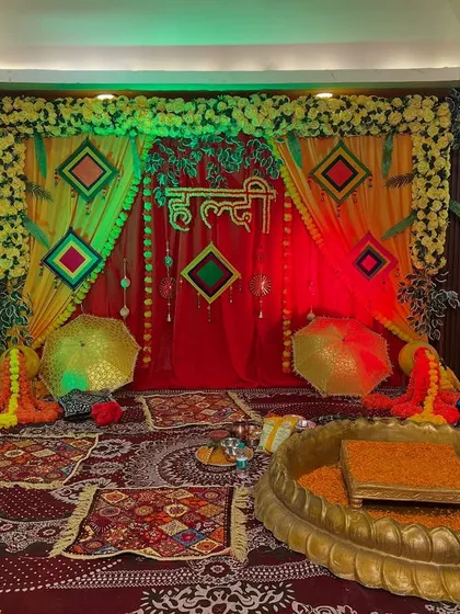 A Haldi ceremony in progress, with the stage decorated in red and yellow drapes, marigold flowers, and colorful lighting.
