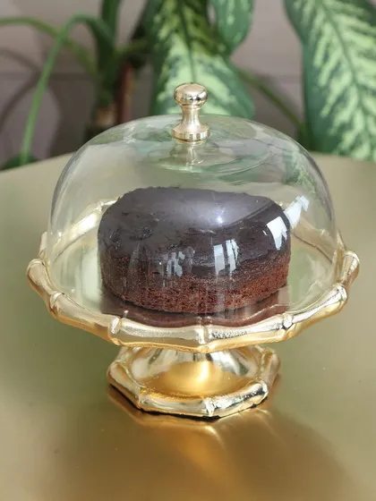The classic Gold Cloche stand with a bamboo-style base, holding a rich chocolate cake. Its timeless design is perfect for any occasion, from birthdays to holiday gatherings.