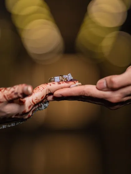 A detailed close-up of the ring exchange. This macro shot focuses on the symbol of their commitment, with a beautiful bokeh background from the event lights.