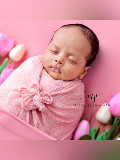 A baby wrapped in a pink swaddle, surrounded by pink and white tulips.