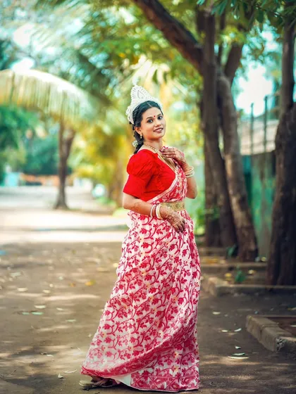 A full length portrait of the bride in a beautiful outdoor setting, showcasing her classic Bengali bridal look.