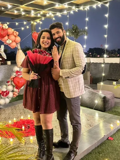 A full-length shot of the happy couple, surrounded by a romantic setup of heart-shaped balloons and fairy lights. This is the picture-perfect ending to a successful surprise proposal.