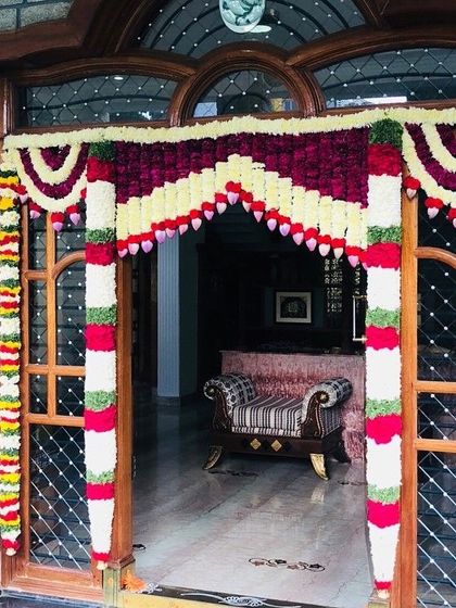 A beautiful floral archway for a main door, made with velvet-red and white flowers in a traditional pattern, perfect for a housewarming.