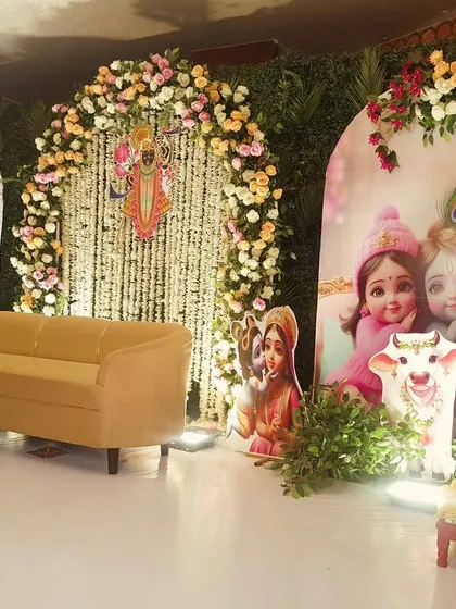 A divine 'Bal Gopal' or baby Krishna themed setup for a celebration. The decor features adorable illustrations of Krishna, surrounded by pastel floral arches and traditional Indian motifs.