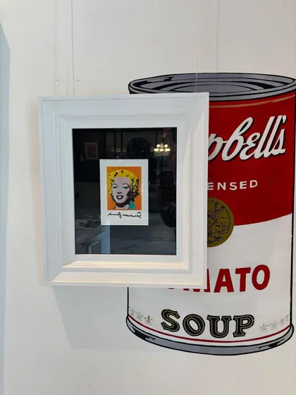 A signed 'Postcard Marilyn' by Andy Warhol, displayed against a giant Campbell's soup can graphic. This is one of the most important artworks of the 20th century and a pioneering piece of pop art.