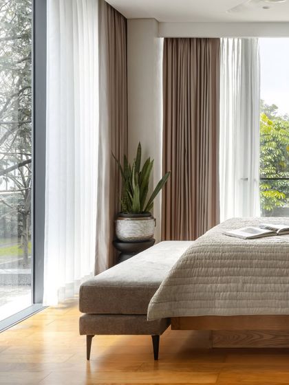 This bedroom is all about the view. We kept the interiors minimal and warm, with a low bed and an upholstered bench, to ensure the focus remains on the floor-to-ceiling windows and the greenery outside.