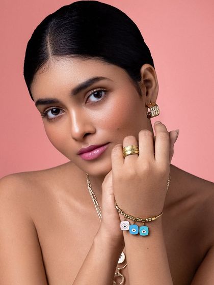 This shot highlights the playful evil-eye charm bracelet, adding a touch of modern trend to the classic gold jewelry look.