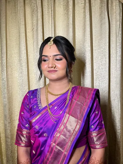 A portrait of a beautiful Maharashtrian bride in a vibrant purple paithani saree. The makeup is kept soft and minimal to let the rich color of the saree and her natural beauty shine.