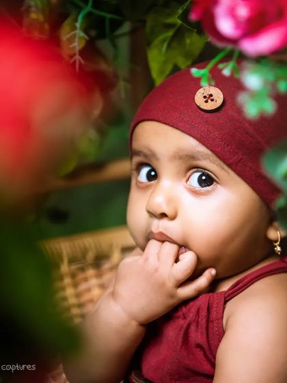 A thoughtful, curious gaze framed by beautiful red flowers. This close-up shot highlights the delicate features and inquisitive nature of a baby.